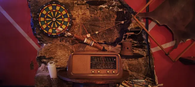 Muro in pietra con un bersaglio per le freccette e una radio antica in legno