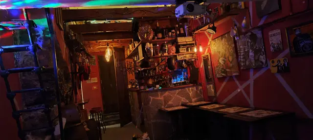La sala principale di Antiche Cappe Rosse: pareti rosse, tavoli alti, bancone in pietra, proiettore e luci colorate sul soffitto